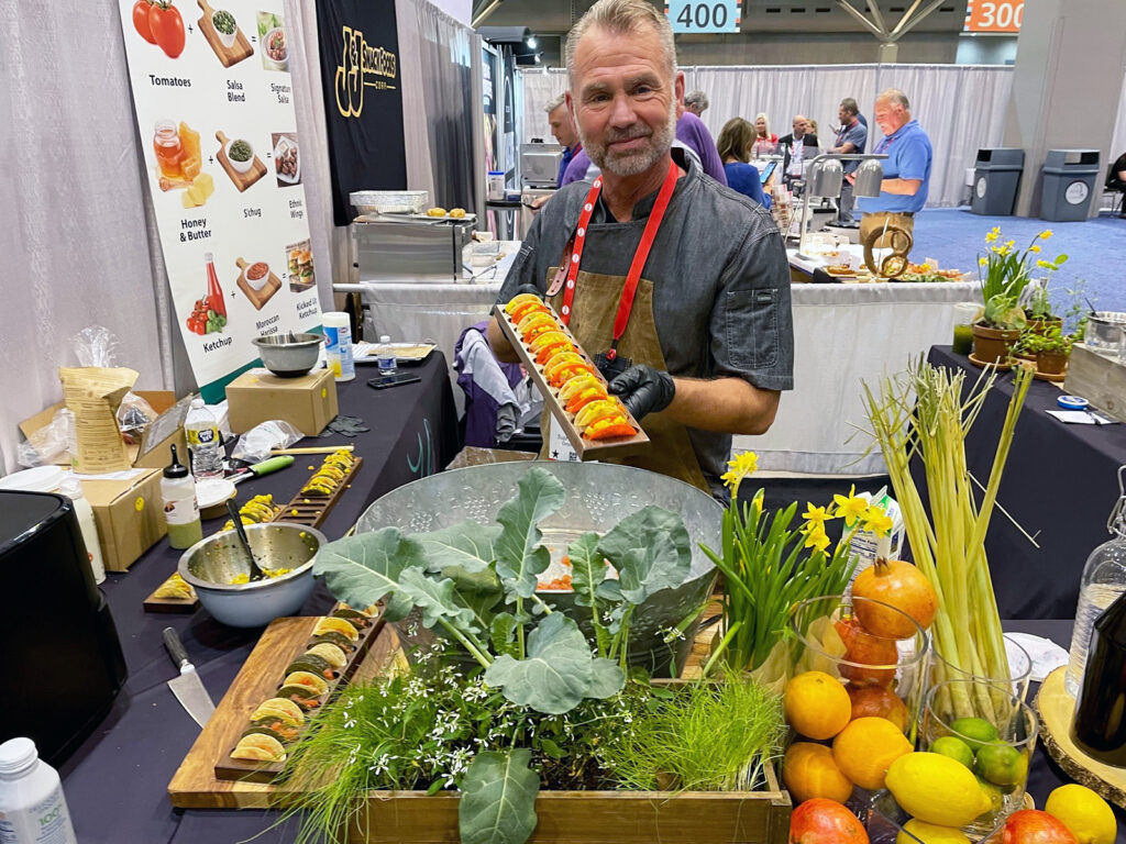 Male chef posing with a platter of mini tacos at a tradeshow